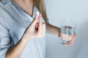 woman holding a glass of water and white medicine pill