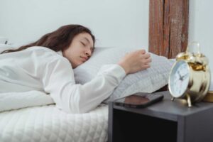 young woman sleeping in bed in morning with alarm clock
